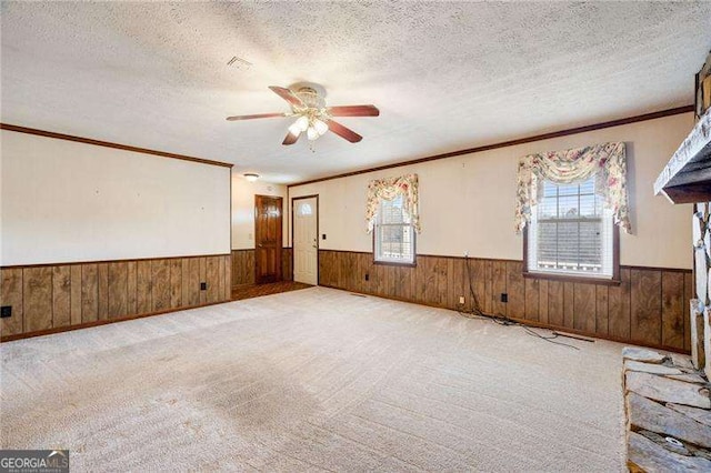 carpeted spare room with ceiling fan, crown molding, wooden walls, and a textured ceiling