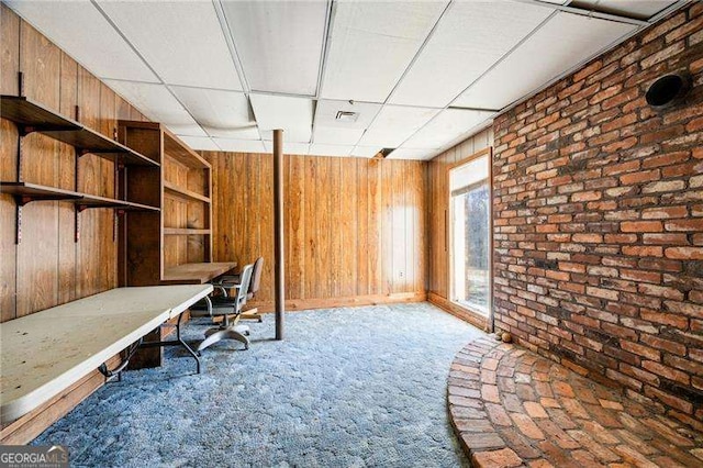 unfurnished office featuring carpet floors, wooden walls, brick wall, and a paneled ceiling