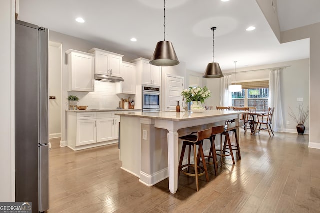 kitchen featuring decorative light fixtures, an island with sink, white cabinets, light stone counters, and stainless steel appliances