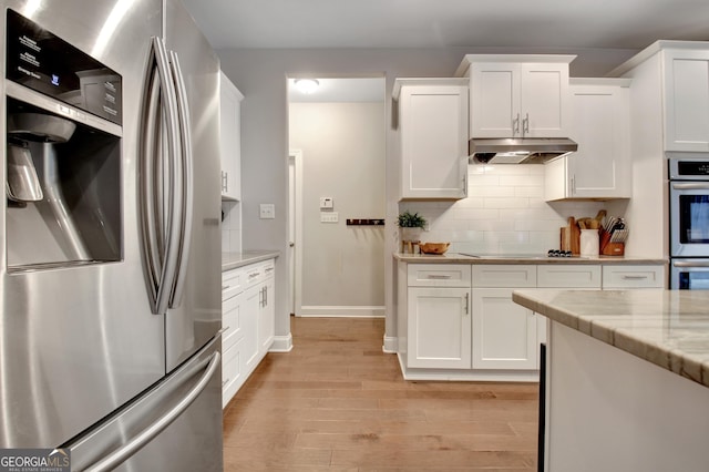 kitchen featuring appliances with stainless steel finishes, light stone counters, white cabinets, decorative backsplash, and light wood-type flooring