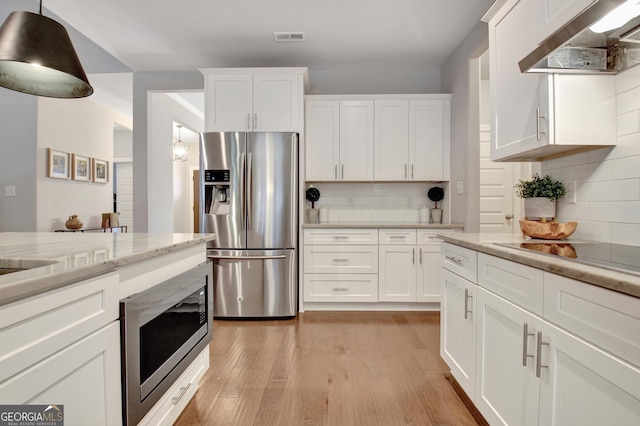 kitchen with white cabinets, light stone counters, light hardwood / wood-style floors, stainless steel appliances, and wall chimney range hood