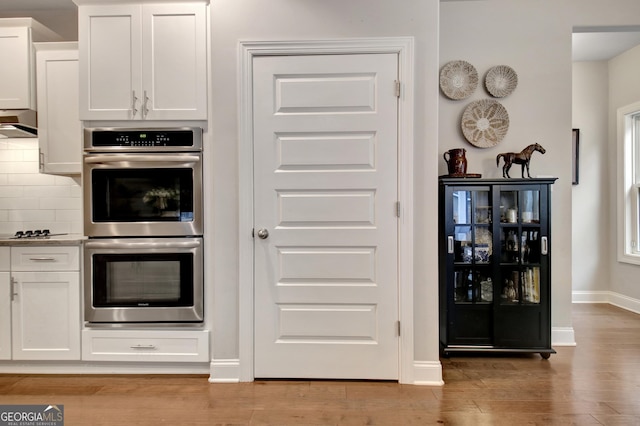 kitchen with tasteful backsplash, double oven, light hardwood / wood-style floors, and white cabinets