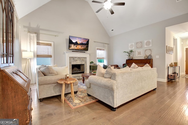 living room with hardwood / wood-style flooring, ceiling fan, a stone fireplace, and high vaulted ceiling