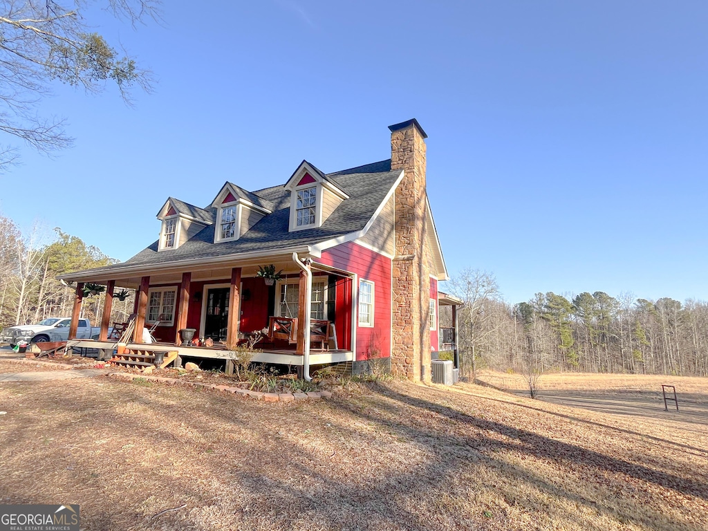 view of front of property with covered porch, a chimney, and central AC unit