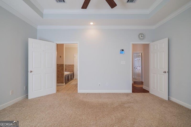 unfurnished bedroom with crown molding, light colored carpet, ensuite bath, and a tray ceiling