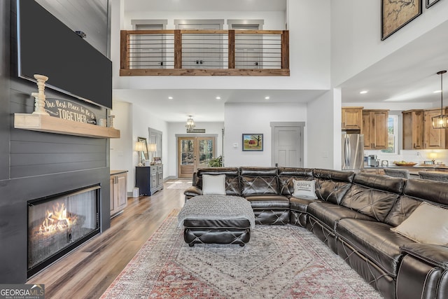 living room with a high ceiling, a large fireplace, french doors, and light hardwood / wood-style flooring