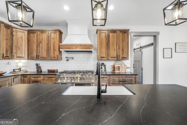 kitchen with range with two ovens, premium range hood, a barn door, and decorative light fixtures