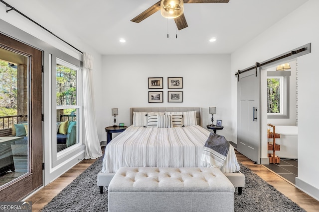 bedroom featuring a barn door, dark hardwood / wood-style floors, access to outside, and ceiling fan