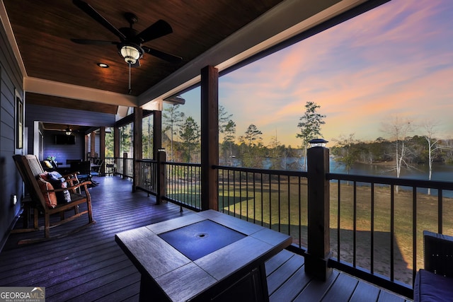 deck at dusk with a water view, ceiling fan, and a lawn