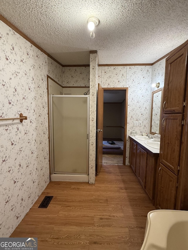 bathroom with crown molding, wood-type flooring, a textured ceiling, vanity, and a shower with door