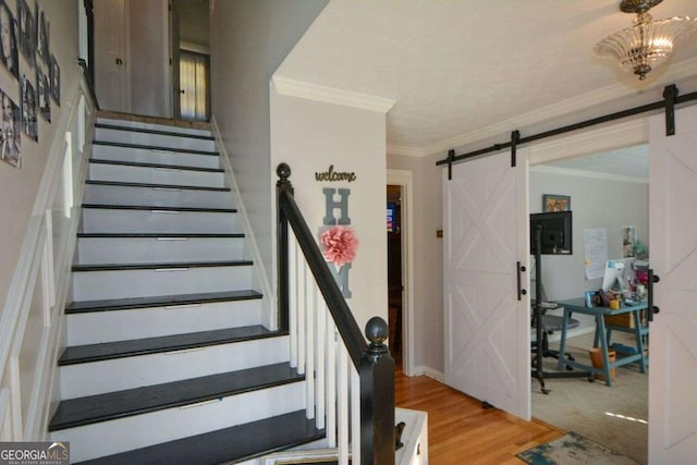 stairway with hardwood / wood-style flooring, ornamental molding, a barn door, and a textured ceiling