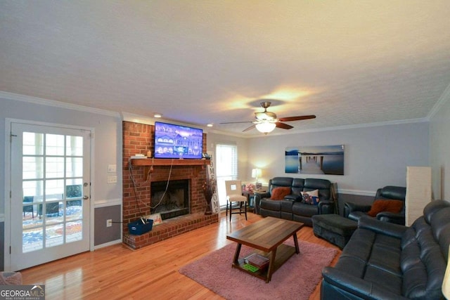 living room featuring ceiling fan, hardwood / wood-style floors, ornamental molding, a textured ceiling, and a brick fireplace