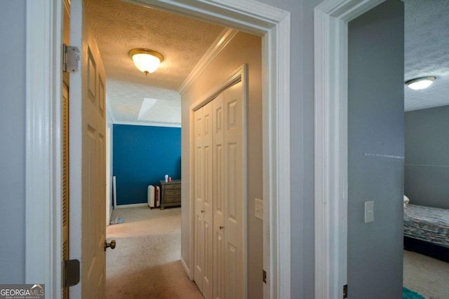 hallway with light colored carpet, ornamental molding, and a textured ceiling