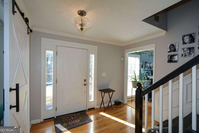 entryway featuring ornamental molding, a barn door, hardwood / wood-style floors, and a wealth of natural light