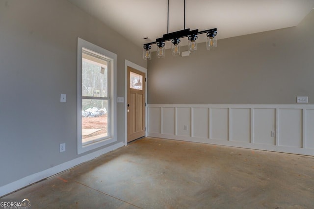 unfurnished dining area featuring a wainscoted wall, concrete floors, and a decorative wall