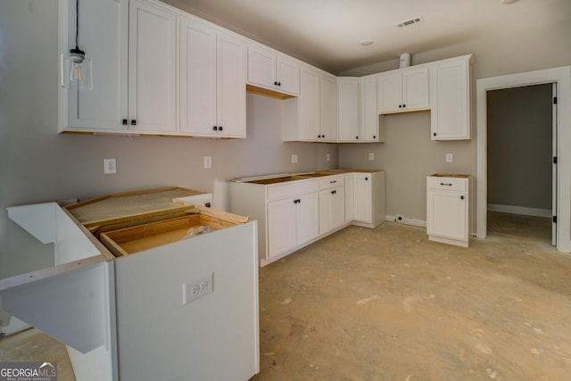 kitchen featuring hanging light fixtures, visible vents, unfinished concrete floors, and white cabinetry