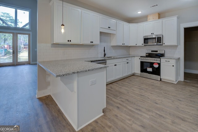 kitchen with visible vents, a peninsula, light wood-style flooring, a sink, and stainless steel appliances