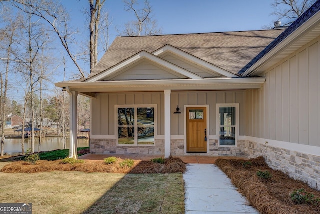 entrance to property with stone siding, covered porch, board and batten siding, and roof with shingles