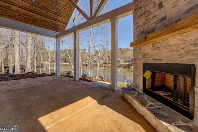 view of patio with a water view and an outdoor stone fireplace