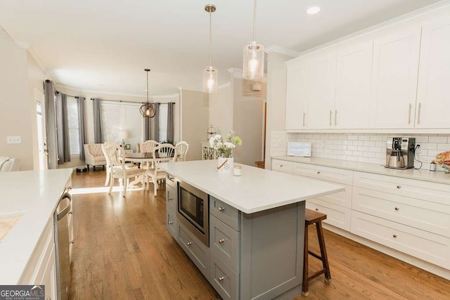 kitchen featuring a kitchen bar, gray cabinetry, hanging light fixtures, appliances with stainless steel finishes, and white cabinets