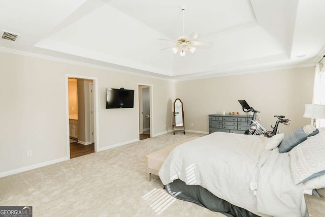 bedroom featuring crown molding, light colored carpet, a raised ceiling, and ensuite bath