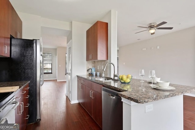 kitchen with dark wood-type flooring, sink, dark stone countertops, stainless steel appliances, and backsplash