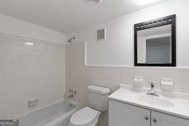 full bathroom with tiled shower / bath, vanity, toilet, and tile walls