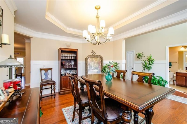 dining area featuring a raised ceiling, wood-type flooring, ornamental molding, and an inviting chandelier