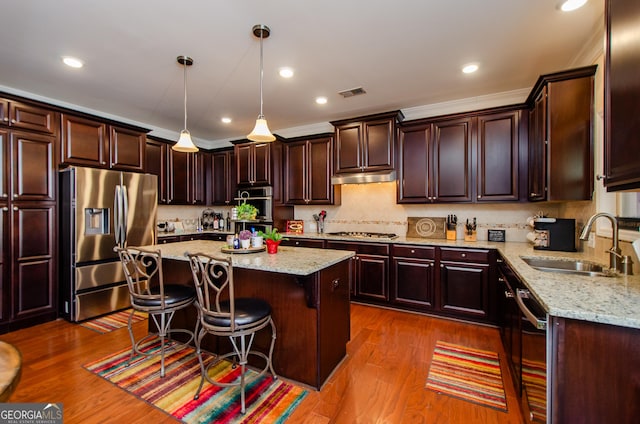 kitchen with pendant lighting, sink, appliances with stainless steel finishes, a kitchen breakfast bar, and a center island