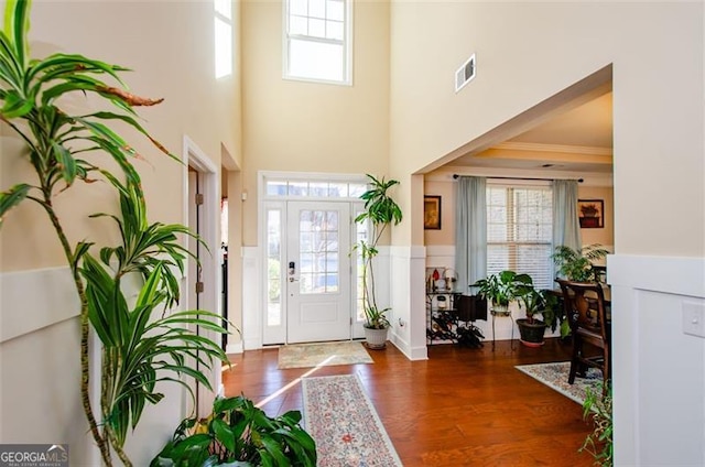 entryway with a high ceiling, ornamental molding, a wealth of natural light, and dark hardwood / wood-style flooring