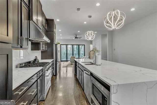 kitchen featuring sink, appliances with stainless steel finishes, hanging light fixtures, a spacious island, and light stone countertops