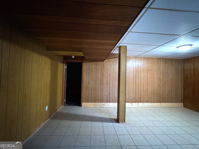 basement featuring wooden walls, a paneled ceiling, and light tile patterned flooring