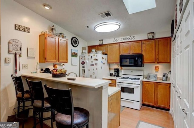 kitchen featuring a breakfast bar, a skylight, kitchen peninsula, white appliances, and light hardwood / wood-style floors