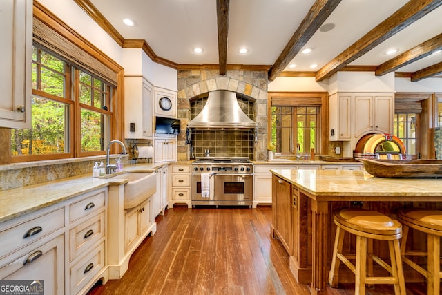 kitchen with backsplash, a kitchen breakfast bar, range with two ovens, light stone counters, and cream cabinetry