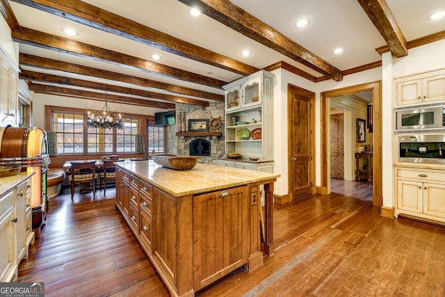 kitchen with pendant lighting, stainless steel appliances, light stone countertops, a kitchen island, and a stone fireplace