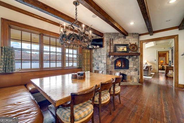 dining area featuring dark hardwood / wood-style flooring, a stone fireplace, beamed ceiling, and an inviting chandelier