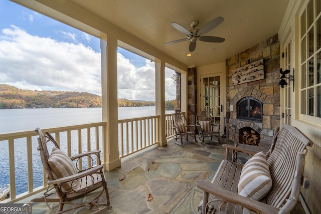 sunroom featuring an outdoor stone fireplace, a water view, and ceiling fan