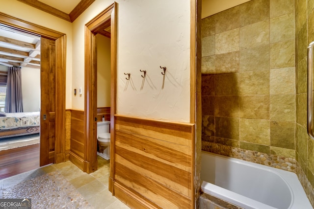 bathroom featuring a bath, ornamental molding, toilet, and wood walls