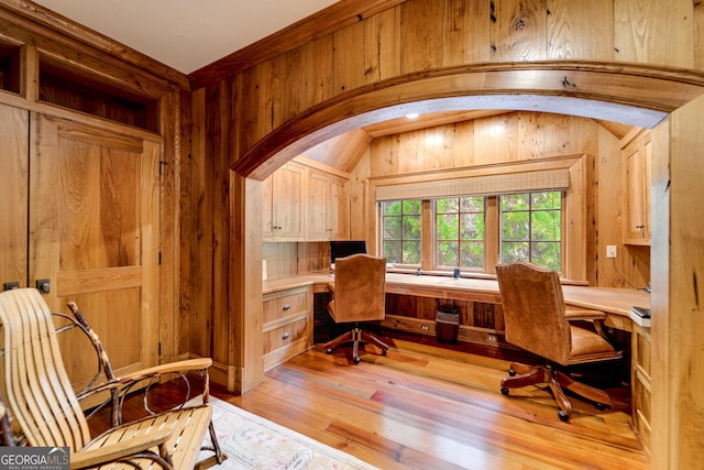 office space with light wood-type flooring, built in desk, vaulted ceiling, and wood walls