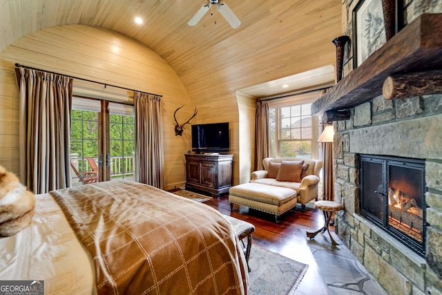 bedroom featuring a stone fireplace, wooden walls, lofted ceiling, dark hardwood / wood-style flooring, and access to exterior