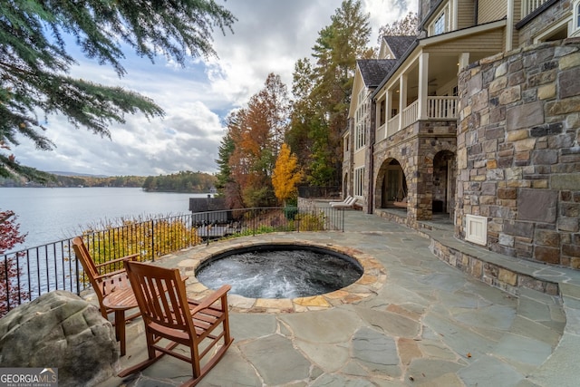 view of patio / terrace with an in ground hot tub, a water view, and a balcony