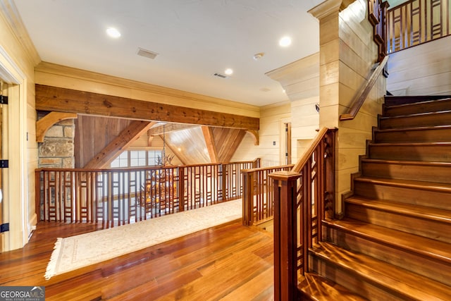 staircase featuring wood-type flooring, ornamental molding, and wooden walls