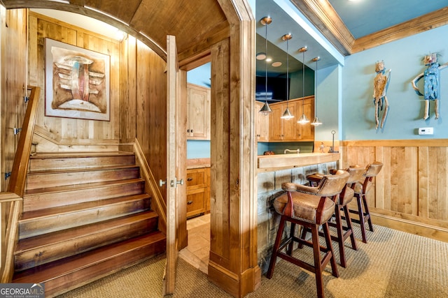 stairway featuring ornamental molding, indoor bar, and wooden walls