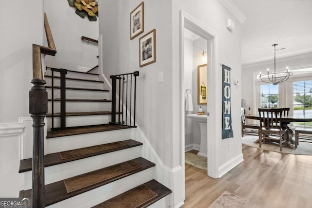 stairway with crown molding, wood-type flooring, and an inviting chandelier