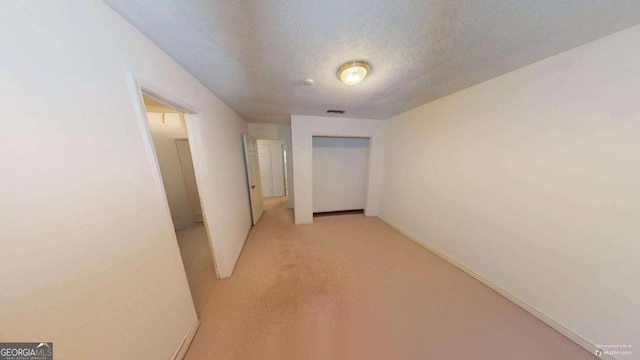 corridor featuring light colored carpet and a textured ceiling