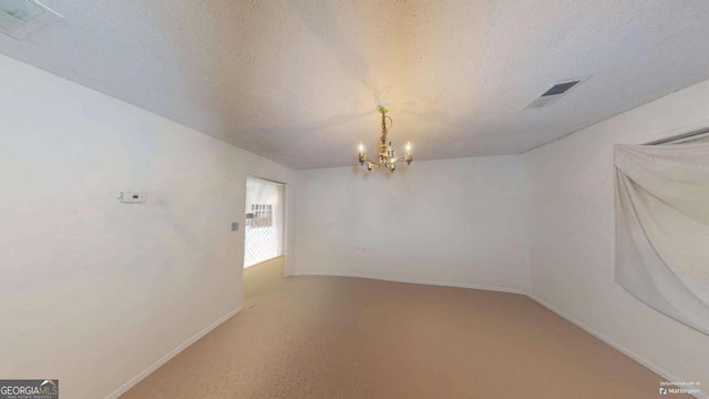 carpeted empty room with a textured ceiling and a notable chandelier