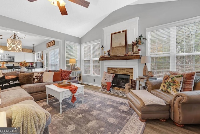 living room with hardwood / wood-style flooring, ceiling fan, a stone fireplace, and vaulted ceiling