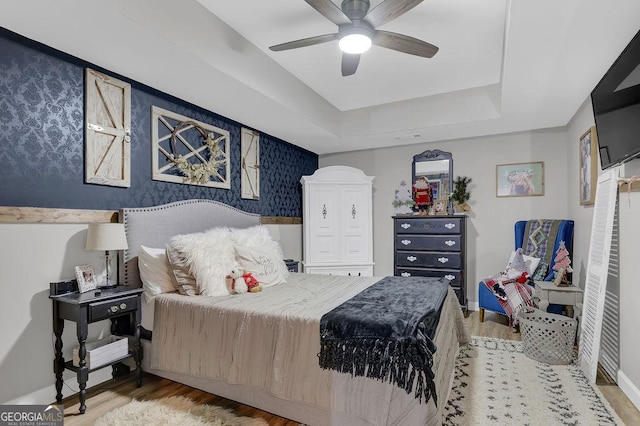 bedroom featuring hardwood / wood-style floors, a raised ceiling, and ceiling fan