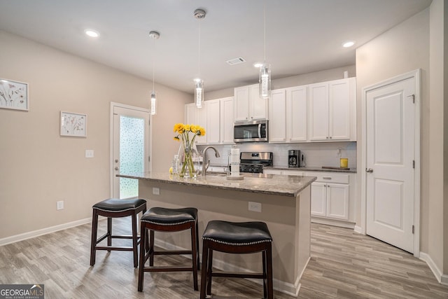 kitchen with stainless steel appliances, an island with sink, white cabinetry, and decorative light fixtures