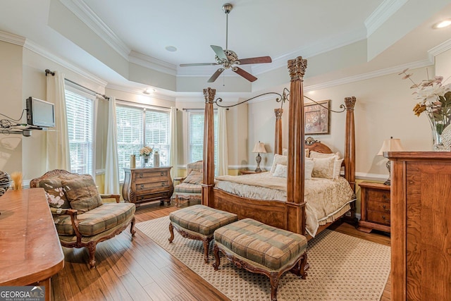 bedroom featuring a raised ceiling, ornamental molding, hardwood / wood-style flooring, and ceiling fan